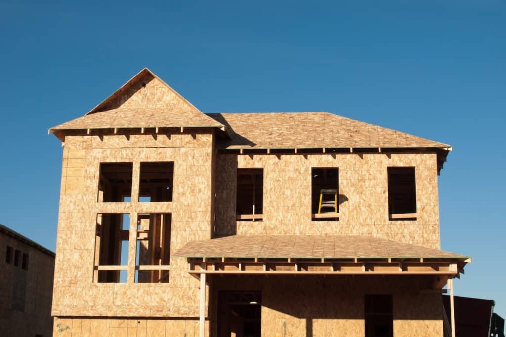 Front exterior of a two-story house under construction, framed with OSB plywood sheathing against a clear blue sky.
