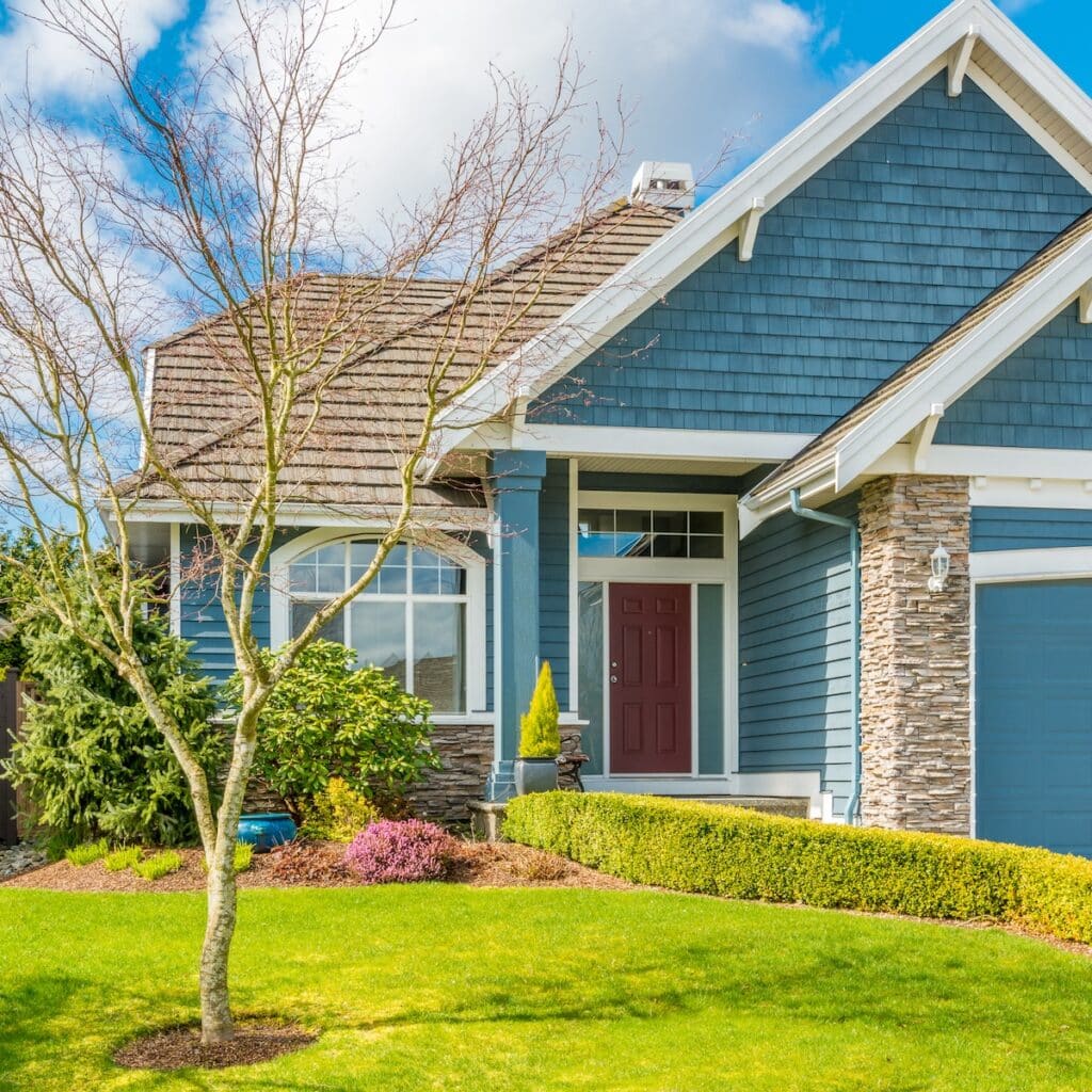 Exterior view of a blue suburban house featuring stone accents, a red front door, and a manicured front lawn.